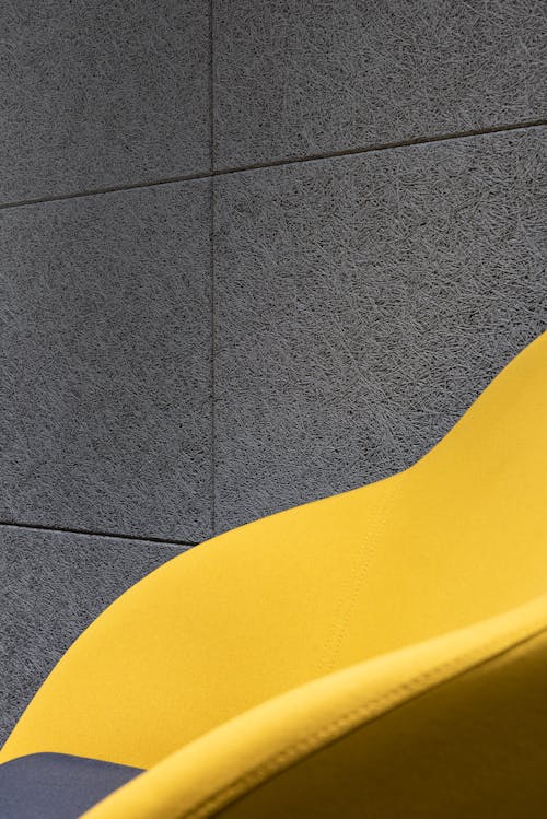 Detail of comfortable bright chair with yellow fabric and cushion placed near gray textured wall in room of modern studio