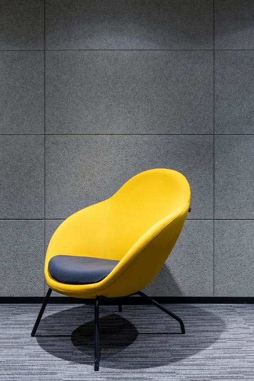 Free Gray pillow on comfortable chair with yellow textile and armrests placed on floor near gray wall in modern light studio Stock Photo