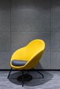 Gray pillow on comfortable chair with yellow textile and armrests placed on floor near gray wall in modern light studio