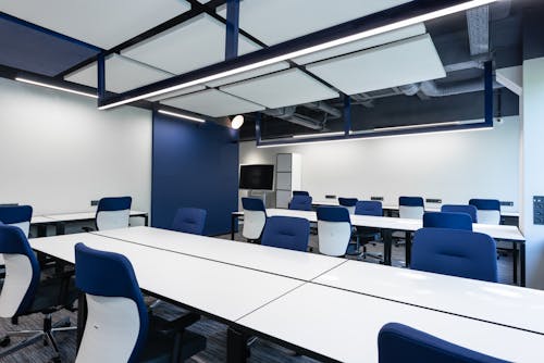 Free Interior of modern spacious workspace with long white tables and blue armchairs placed near monitor with black screen in business center Stock Photo