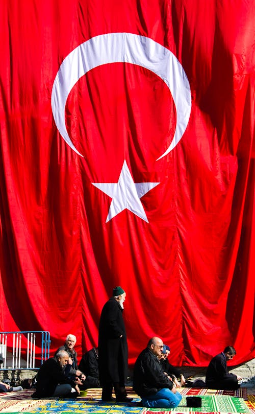 Men Sitting on Rugs in front of a Huge Turkish Flag 