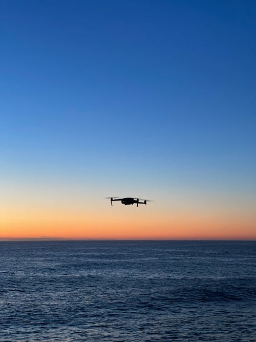 Silhouette of Drone Over the Ocean under Blue Sky