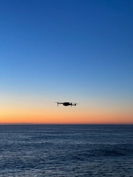 A silhouette of a drone flying over the ocean during a vibrant sunset in Tamarama, NSW.