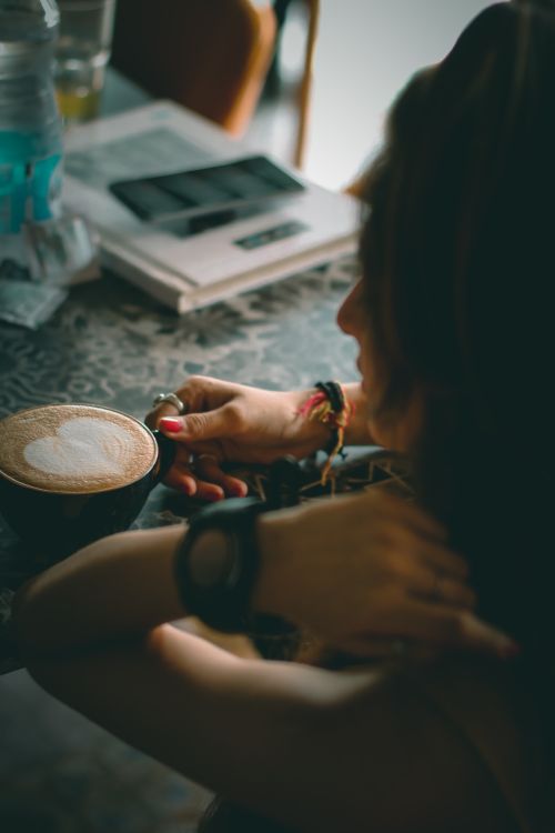 Free A person enjoys a latte with heart art in a cozy indoor café environment. Stock Photo