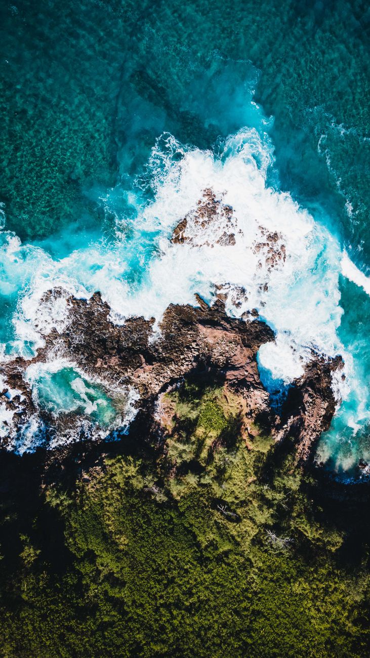 Stunning aerial shot of waves crashing against rocky shoreline, showcasing nature's power.