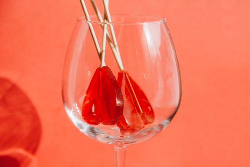 Free Vibrant heart-shaped lollipops arranged inside a wine glass against a bold orange background. Stock Photo