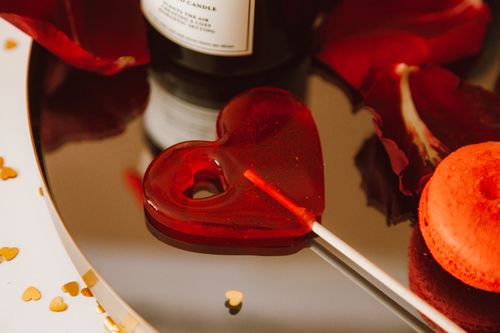 Free Heart-shaped red lollipop with rose petals and gold hearts, perfect for Valentine's Day themes. Stock Photo