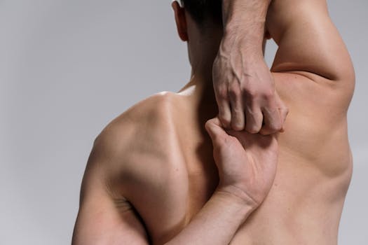 Shirtless muscular man practicing a yoga stretch with hands clasped behind back on a white background.