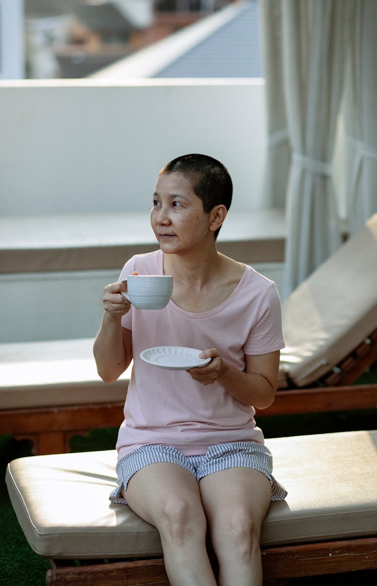 Dreamy Ethnic Woman Resting On Lounger On Terrace And Drinking Coffee