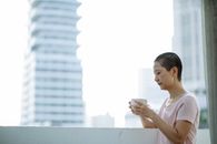 Melancholic adult Asian woman drinking beverage on terrace in sunny morning