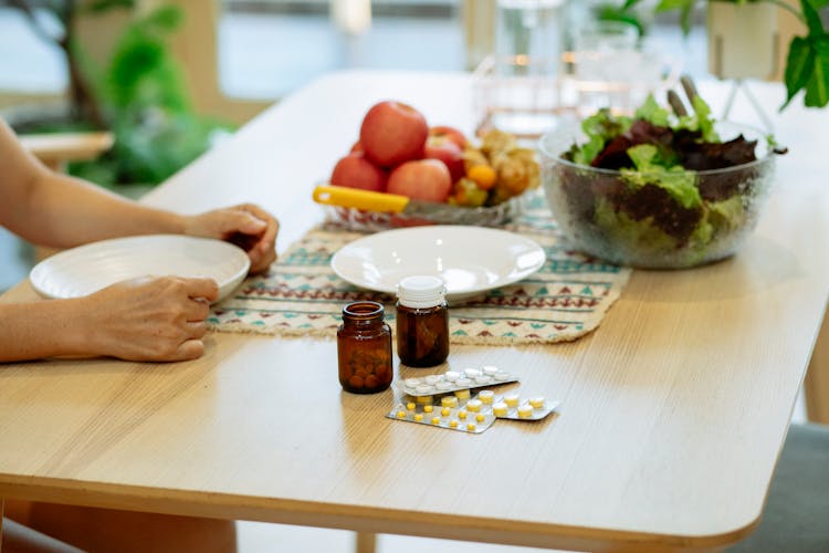 Medicament And Fresh Fruits And Veggies Placed On Table Near Unrecognizable Person