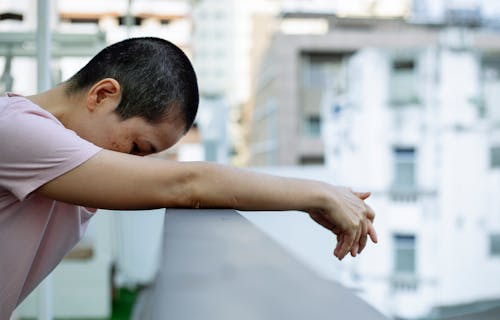 Sad ethnic female leaning forward on railing of terrace and looking down