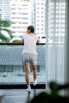 Woman in casual wear looking from an indoor balcony with a city view.