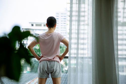 Free Back view of anonymous short hair ill female with hands on waist resting on balcony in hospital Stock Photo