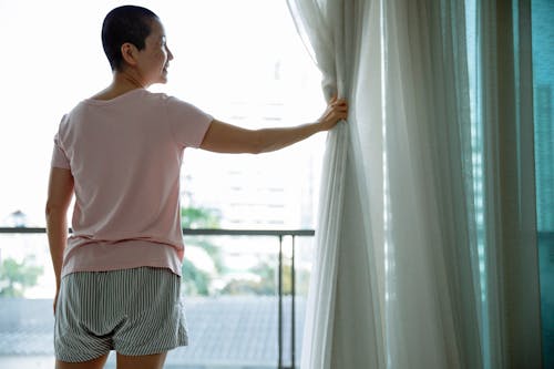Happy Asian woman with short hair opening curtains of window