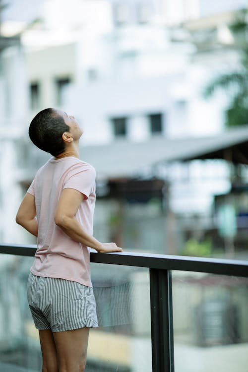 Slender woman suffering from cancer leaning on railing of balcony