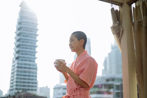 Free Side view of ill ethnic female with short hair and hot tea resting on balcony at home in daylight Stock Photo