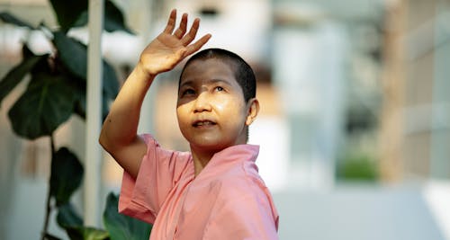 Sick ethnic short haired female in pink robe hiding face on blurred background of street