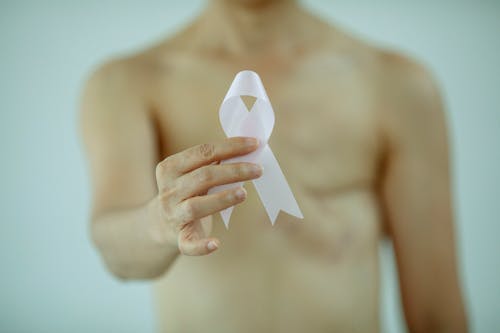 Crop faceless topless lady with pink ribbon in hand with scar on chest after breast removal surgery from cancer standing in bright studio on white background
