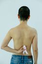 Back view of topless female with short hair standing on white background with hand behind back and holding pink ribbon