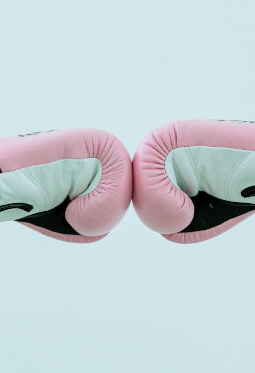 Side view of crop faceless people in pink boxing gloves giving fist bump in bright studio on white background