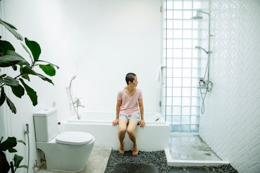 A woman sits pensively on a bathtub in a minimalist white bathroom, suggesting serenity and introspection.