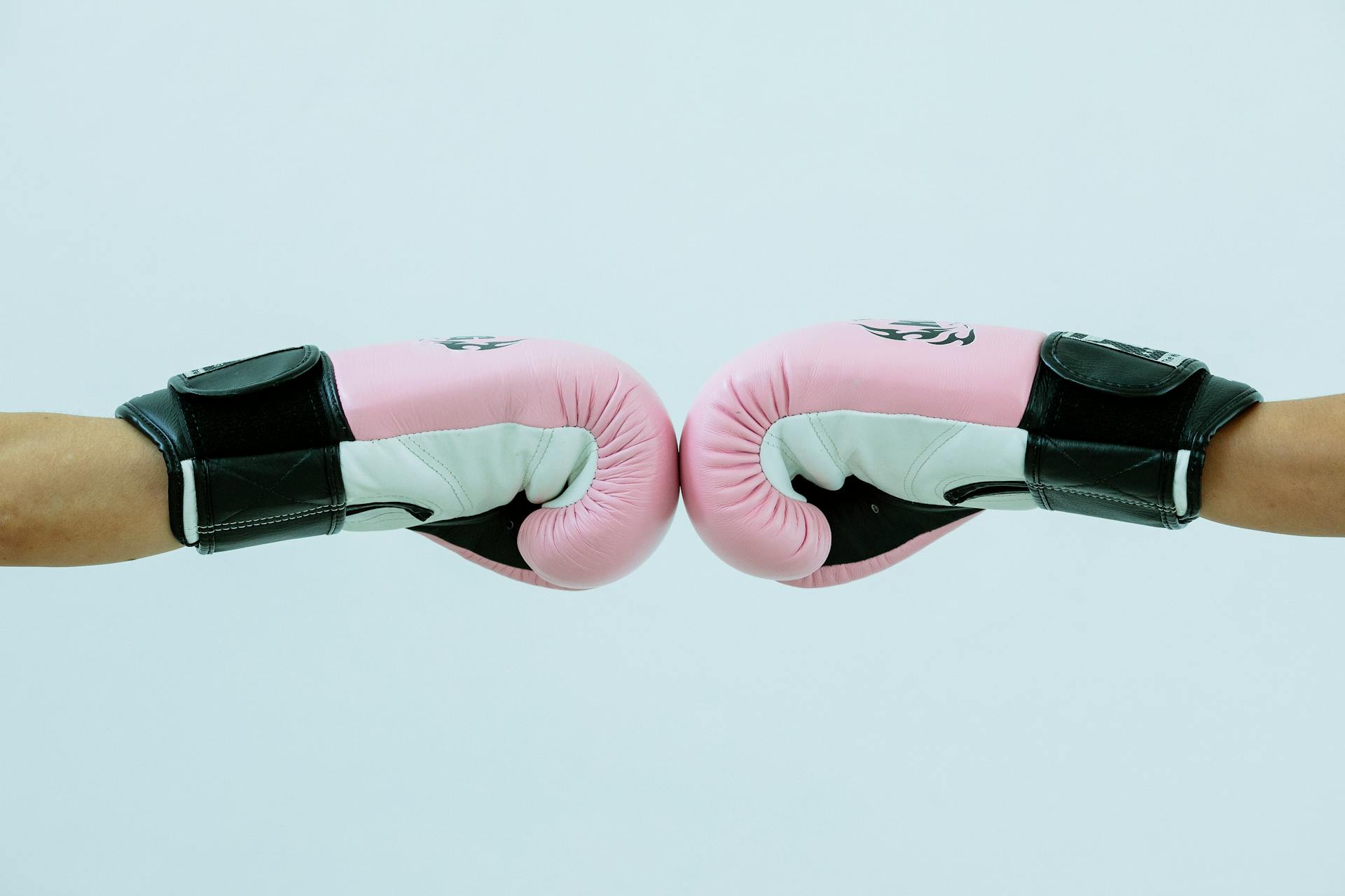 Side view of crop anonymous boxers in pink boxing gloves giving fist bump on white background in light studio