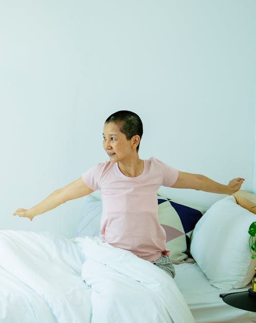 Positive ethnic woman sitting in bed and stretching arms