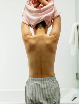 Back view of anonymous person with short dark hair taking off t shirt in light room
