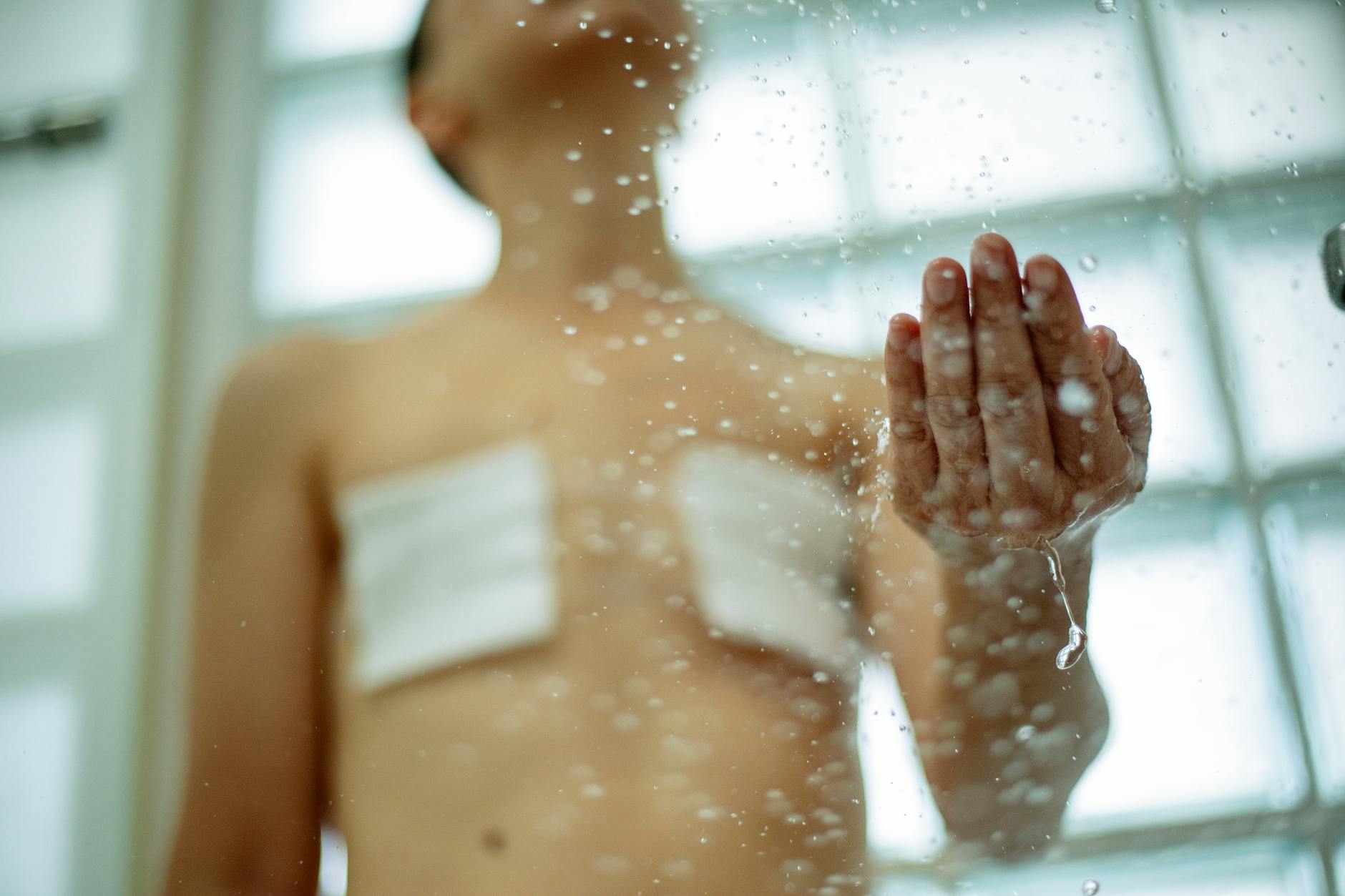 A person with bandages and scars in the shower, illustrating self-care and recovery.