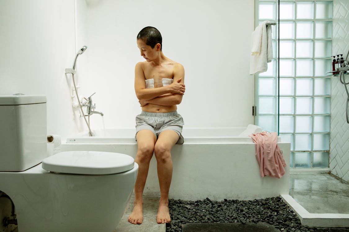 Pensive female with bandages on breast sitting on bath in light bathroom ·  Free Stock Photo