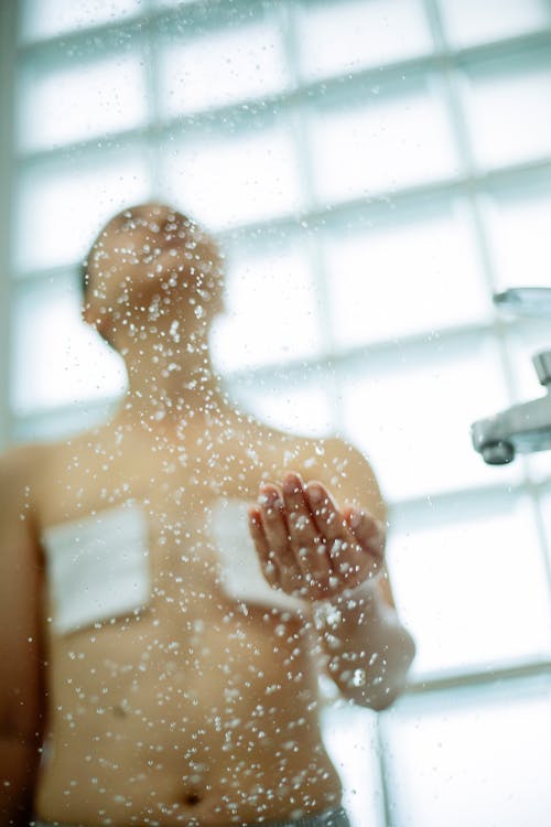 Free From below of anonymous sick female with short hair under drops of water in shower Stock Photo