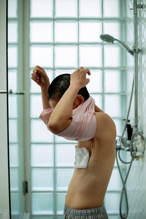 Side view of ill anonymous female wearing T shirt in bathroom with shower in bright daylight