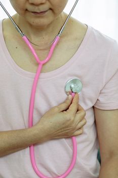 Crop anonymous serious middle age female in casual outfit using pink stethoscope on chest in bright house
