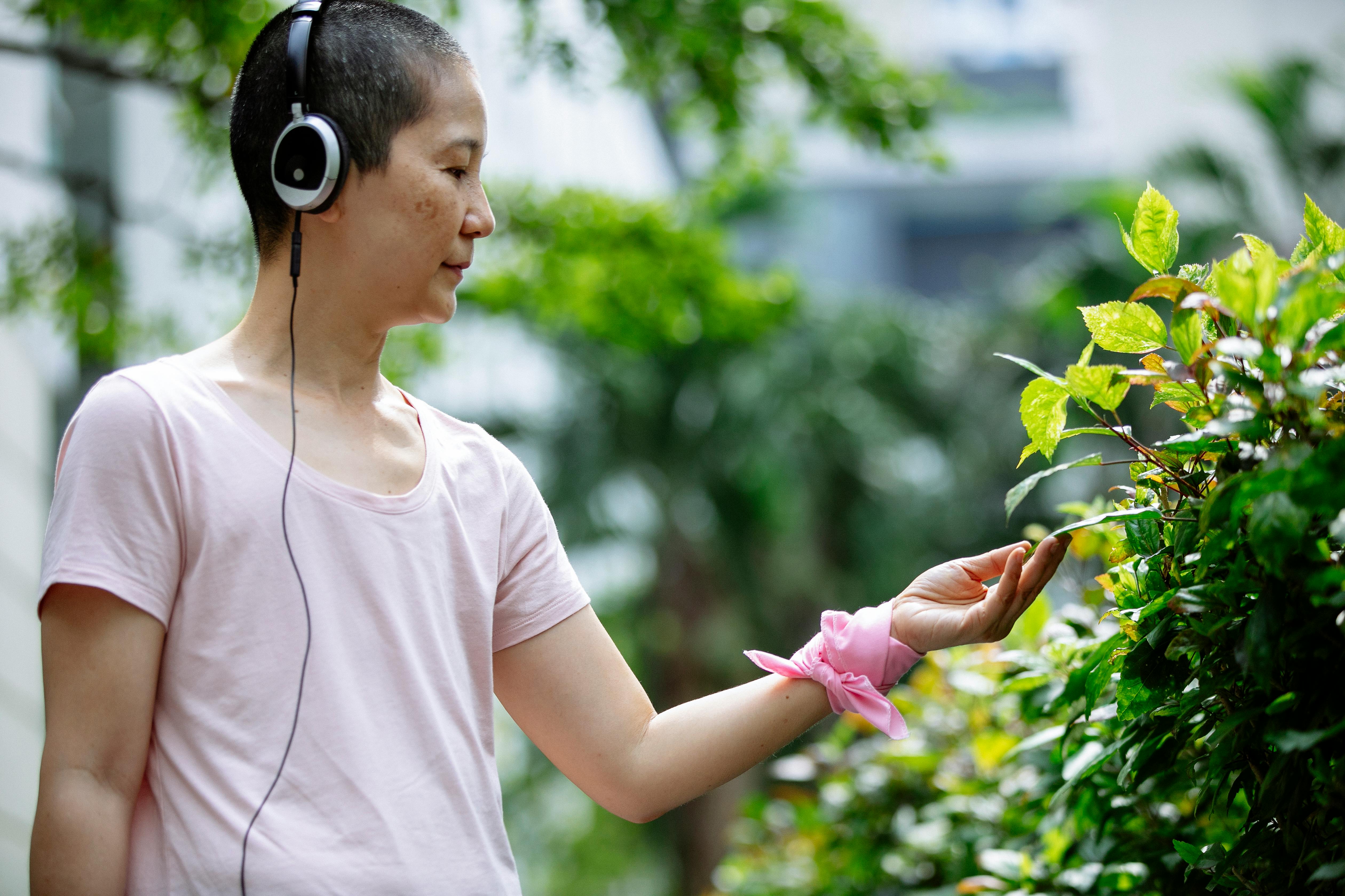 asian lady in headphones examining green plants in street