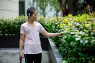 Asian lady in headphones with phone near bushes in street