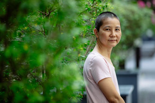 Smiling ill ethnic female with short hair suffering from cancer on blurred background of verdant trees