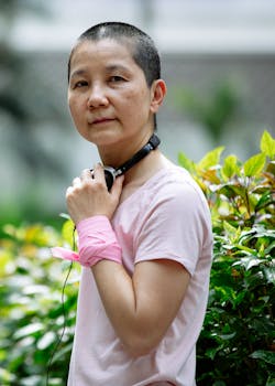 Portrait of an Asian woman with short hair standing in a lush green park with headphones around her neck.