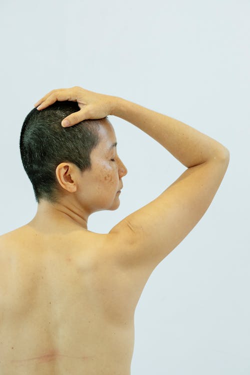 Back view of ethnic shirtless female with eyes closed on white background of studio