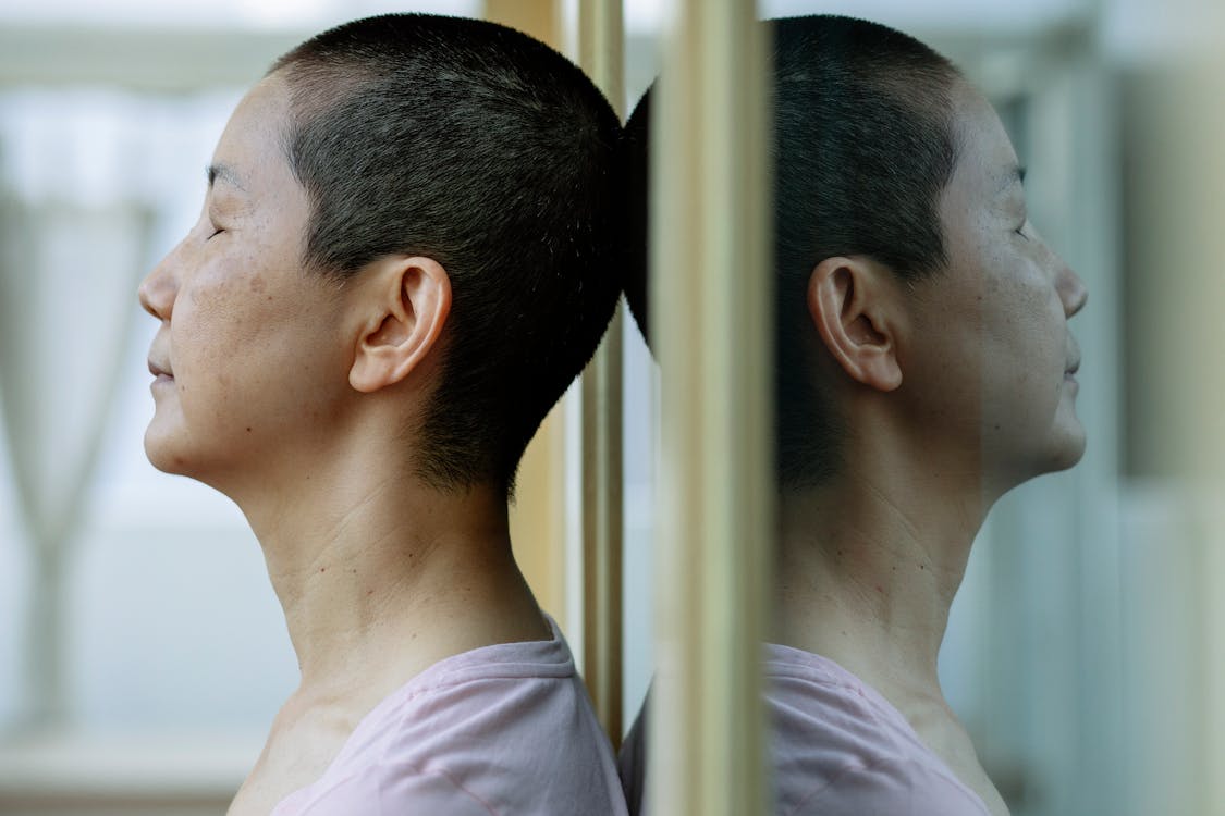 Side view of ethnic ill female with short dark hair leaning on mirror at home