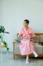 Full body of ethnic ill female with short hair and book pondering and looking away on couch