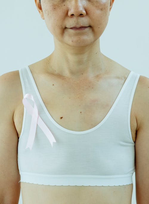 Woman in white top with pink ribbon as sign for Breast Cancer Day
