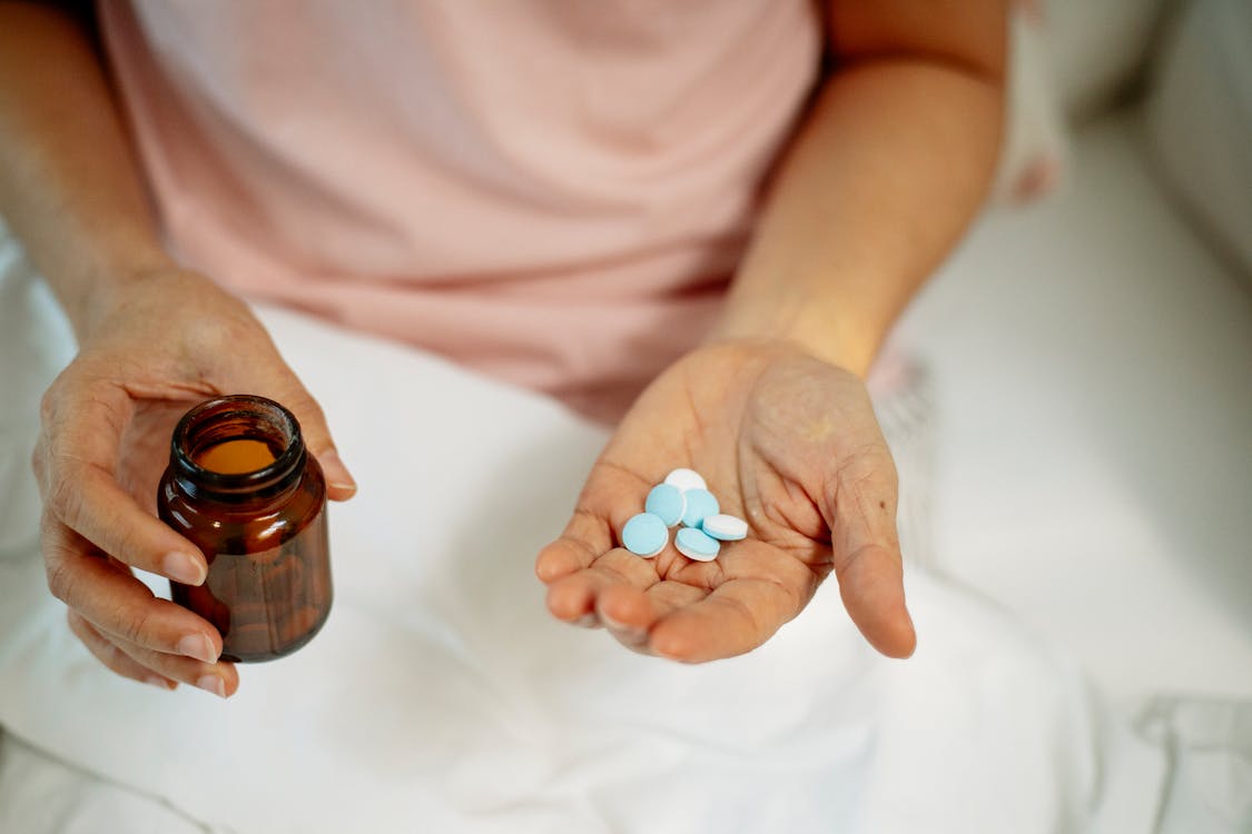 Free Person holding pills in hand while sitting on bed Stock Photo