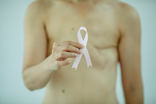 Crop anonymous female with breast cancer showing ribbon on white background of studio