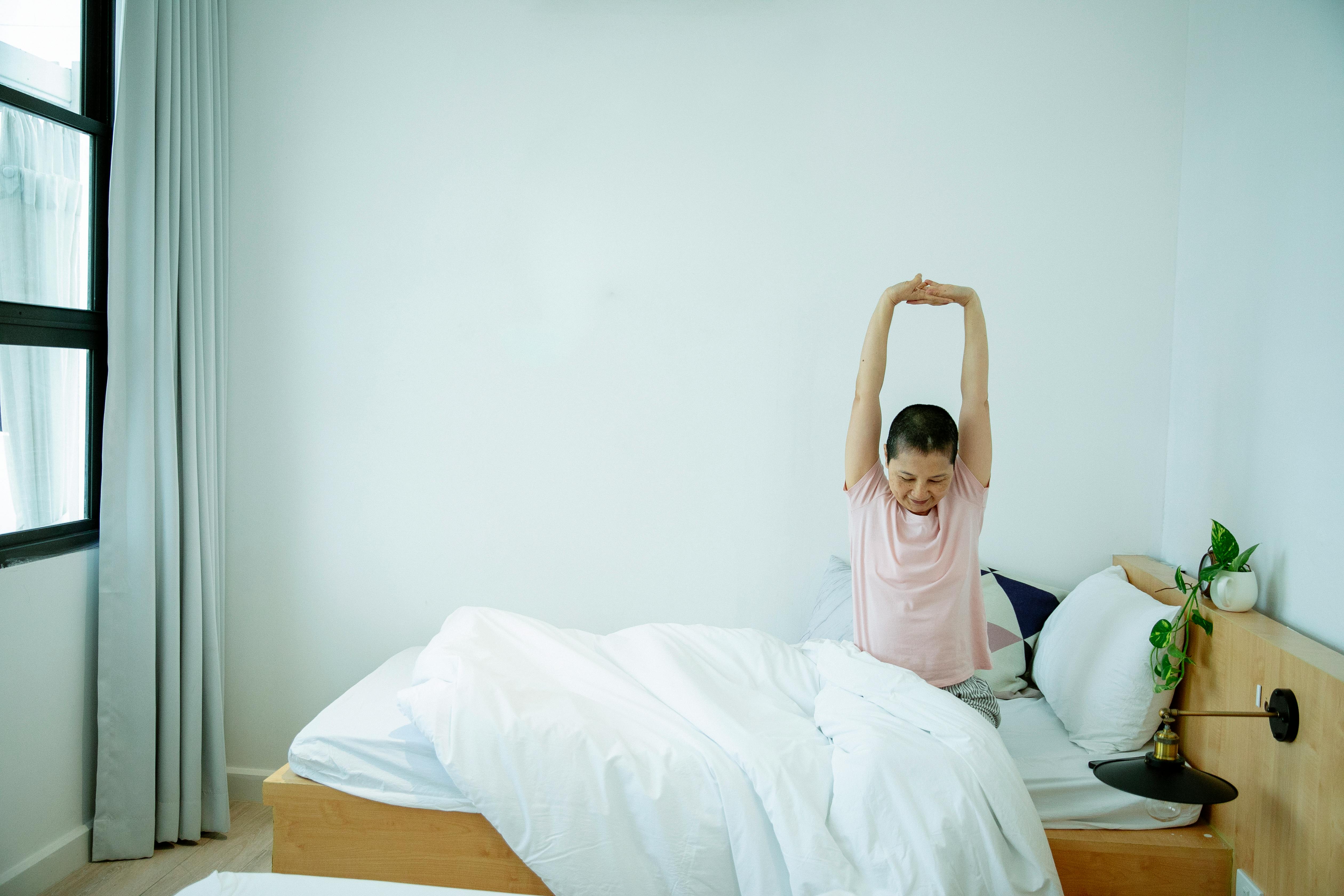 ethnic female stretching body on bed in morning