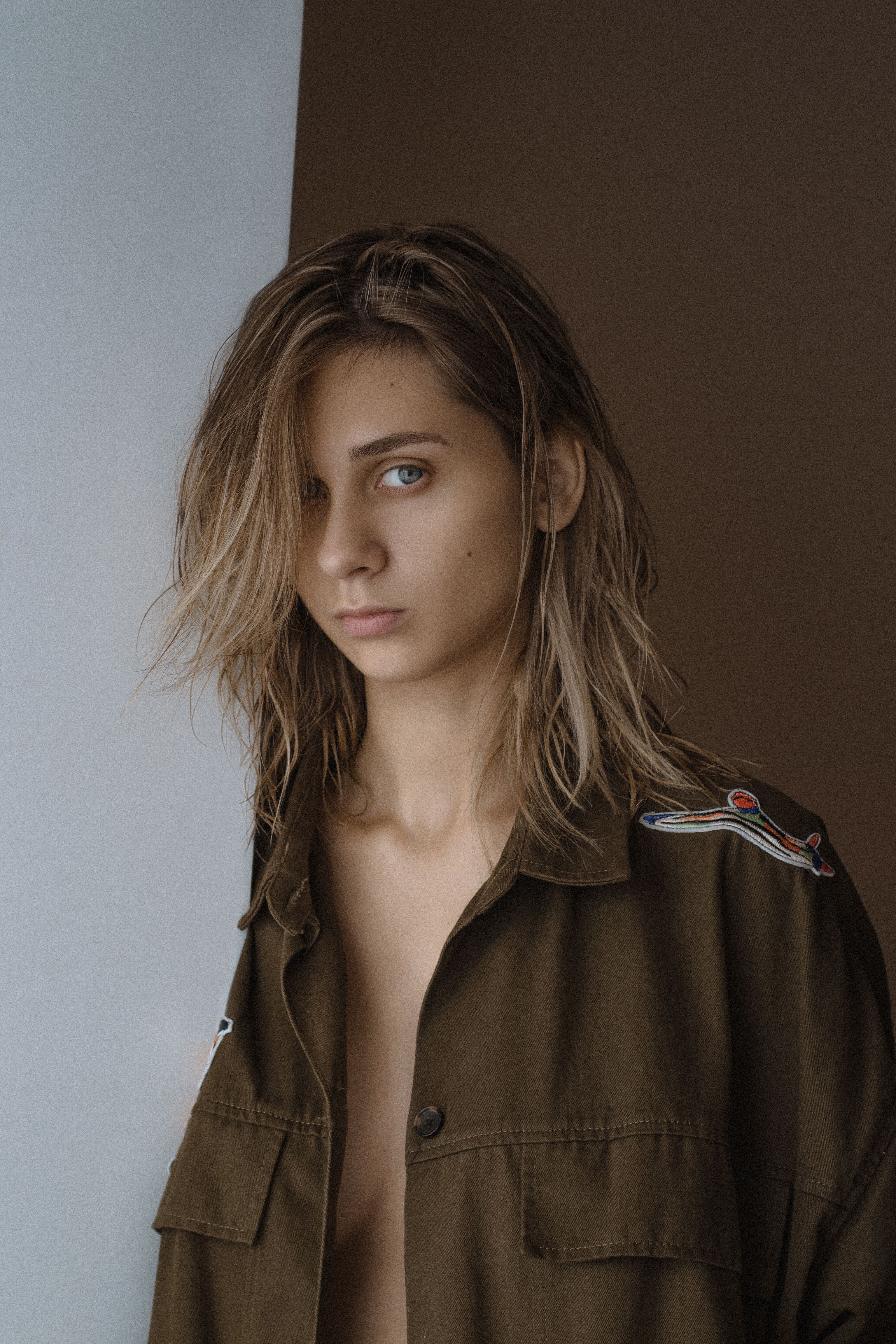 Young woman with wet hair leaning against a white and brown wall, wearing a green jacket.