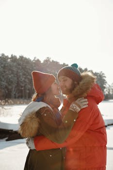 A loving couple shares a cozy embrace outdoors in a snowy, winter landscape.