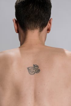 Close-up of a man's back featuring an Om symbol tattoo under natural light.