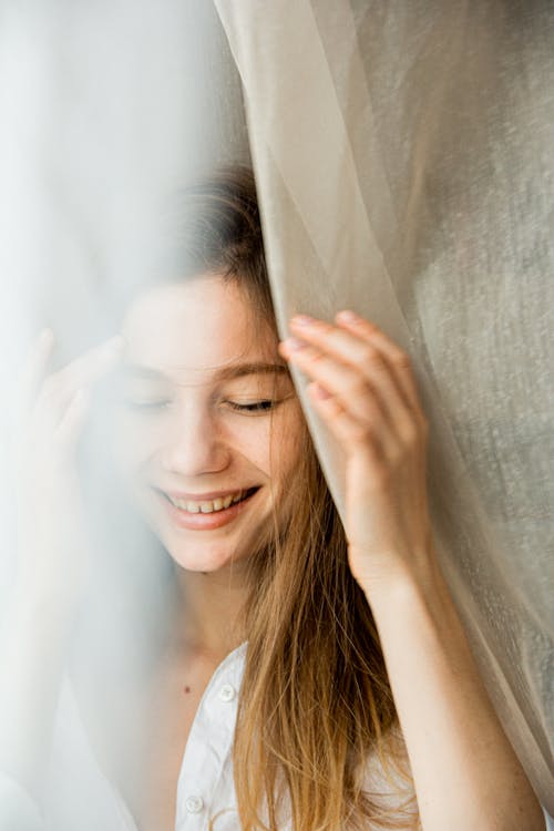 Free A Woman Smiling Near A Sheer Curtain Stock Photo