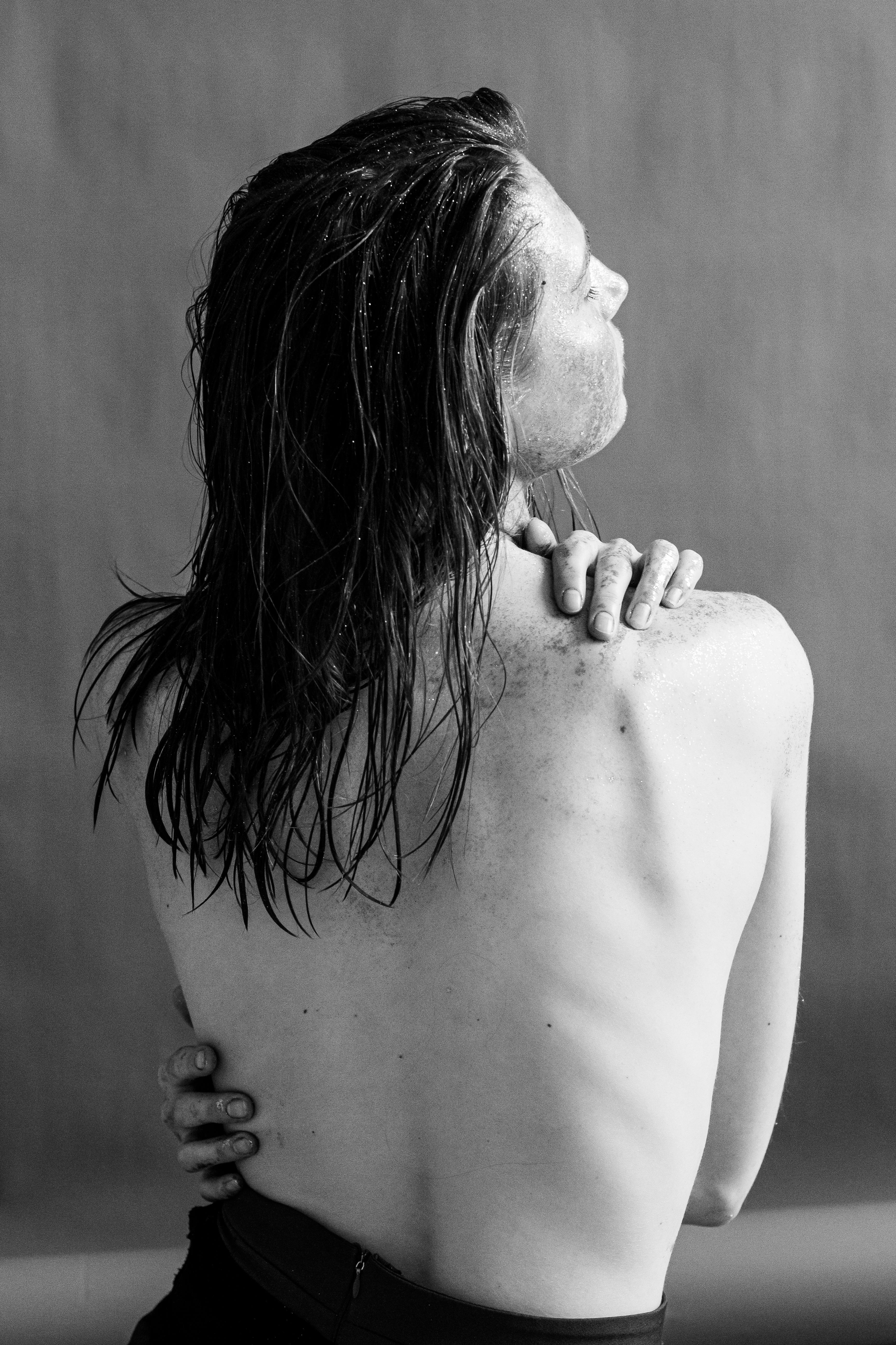 grayscale photo of a woman with a bare back hugging self